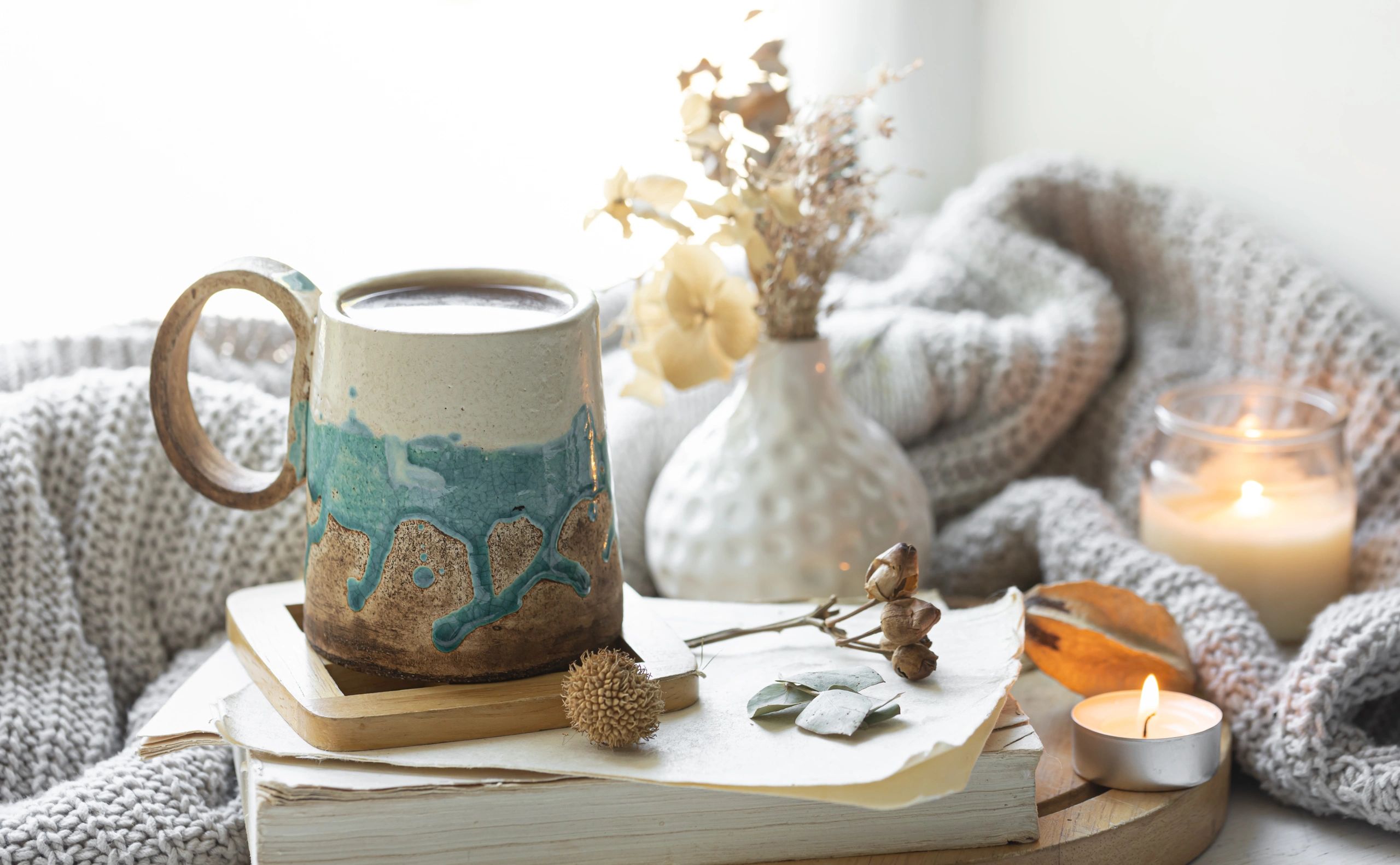 Cozy home autumn composition with a cup, books, candles and a knitted element.