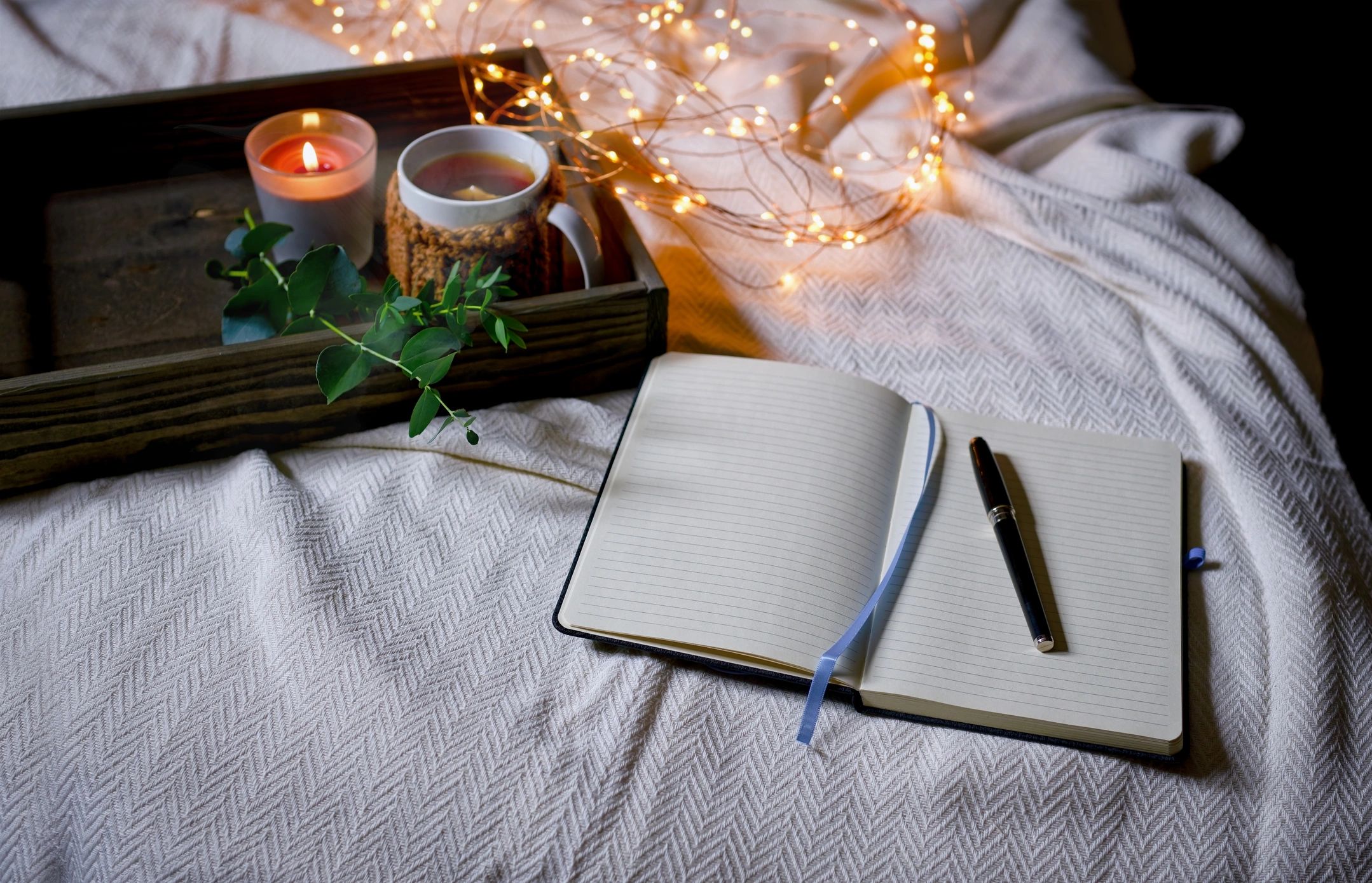 Writing in a journal on a cozy bed next to a warm mug of tea and a burning candle